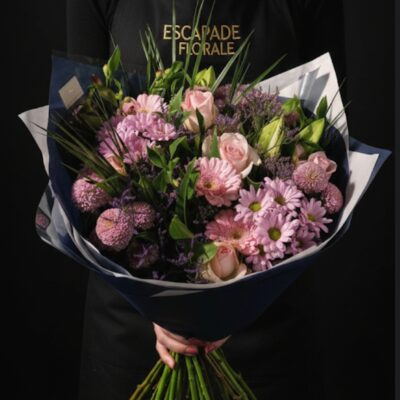 Bouquet "Douceur Locale" ​L'Esprit de la Création ​Un bouquet rond tout en délicatesse qui célèbre la poésie des teintes pastel. Cette composition harmonieuse mêle différentes variétés de fleurs roses et blanches pour un rendu vaporeux et romantique. Idéal pour exprimer une pensée affectueuse, célébrer une fête ou simplement apporter une touche de sérénité à votre intérieur. ​Détails de la Composition ​Cette création privilégie la qualité et la fraîcheur grâce à une sélection de végétaux issus de notre production locale : ​Fleurs Majeures : Élégantes roses roses, germinis rose tendre et lys blancs majestueux pour le parfum et l'éclat. ​Fleurs de Remplissage : Bonny rose et Santini roses pour la générosité, accompagnés de limonium mauve pour une note champêtre et texturée. ​Le Feuillage : Un écrin de verdure sélectionné selon la récolte du moment sur notre terrain de Roncq pour souligner les couleurs pastel.